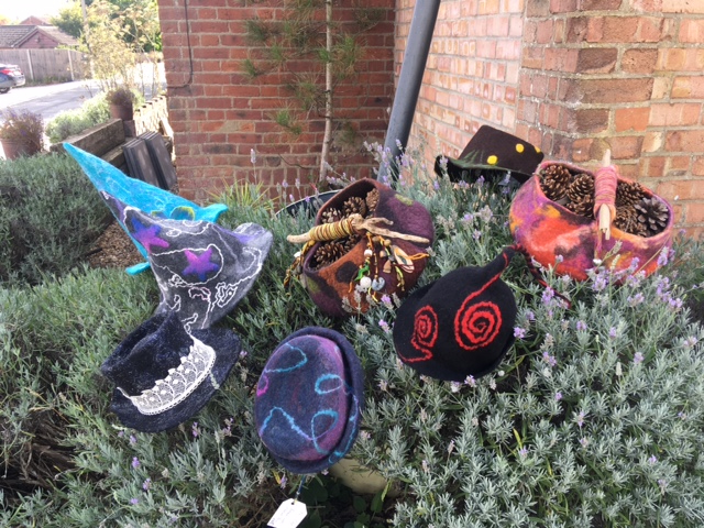 Five felt hats and two felt foraging baskets placed on top of a lavender bush, with a house wall, drain pipe and street behind. Picture by Hazel Nettles.