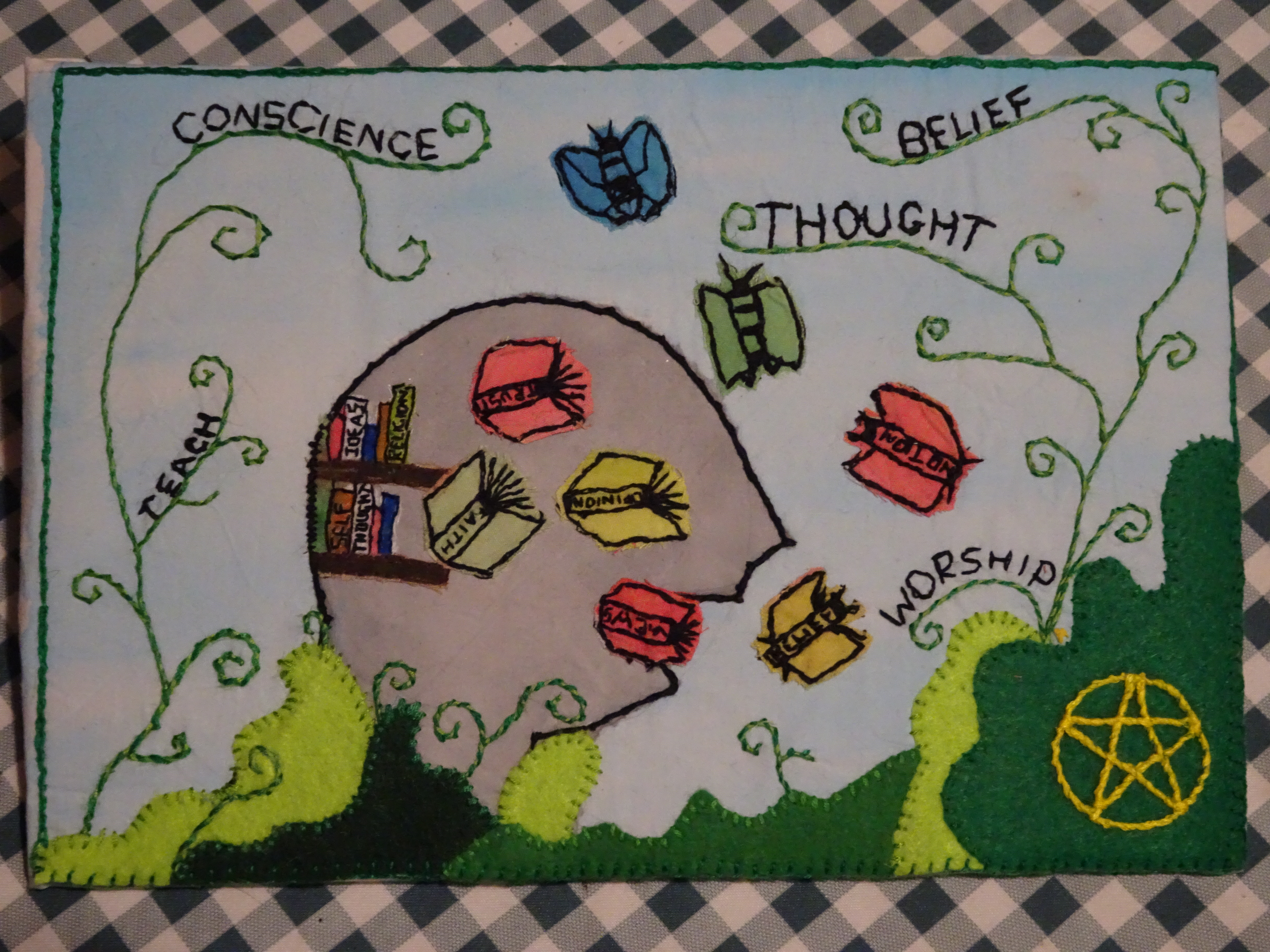 Quilt panel depicting Article 9 of the European Convention on Human Rights, with a picture of a head and book-like butterflies, with the words, 'teach, 'belief', 'thought' and 'worship'.